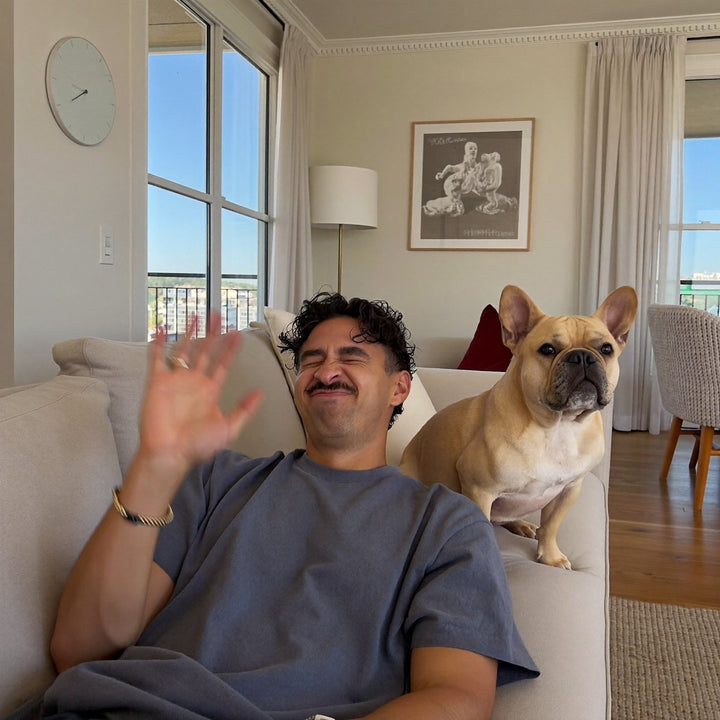 Man waving the air next to his French bulldog on the sofa