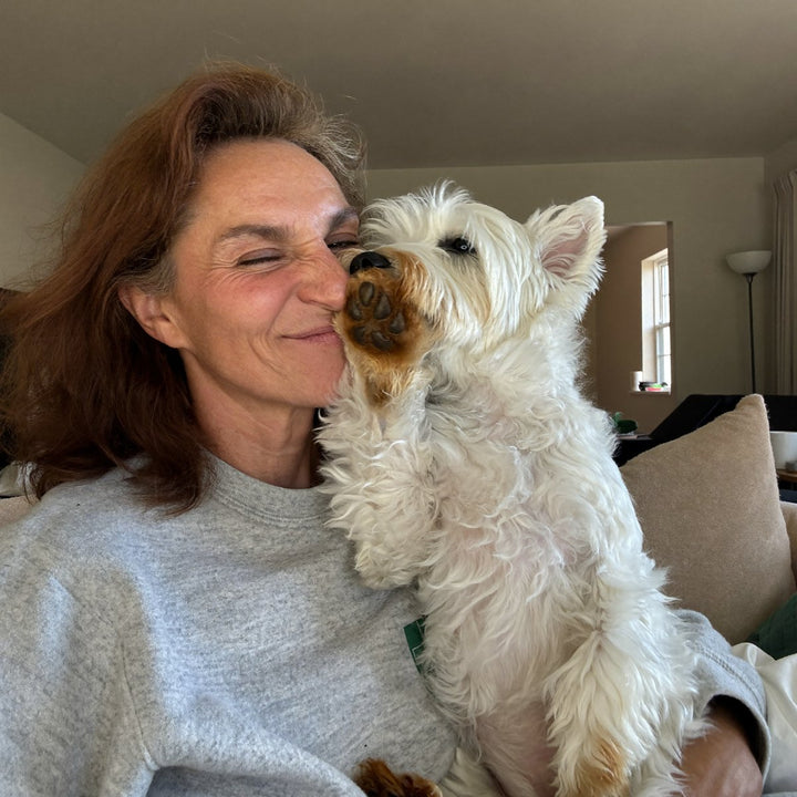Woman on the couch sniffing her westie's paw and pulling a face