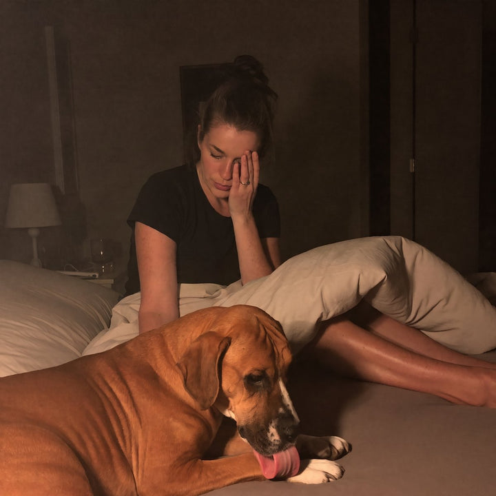 Exhausted woman in bed at night while her boxer licks his paw